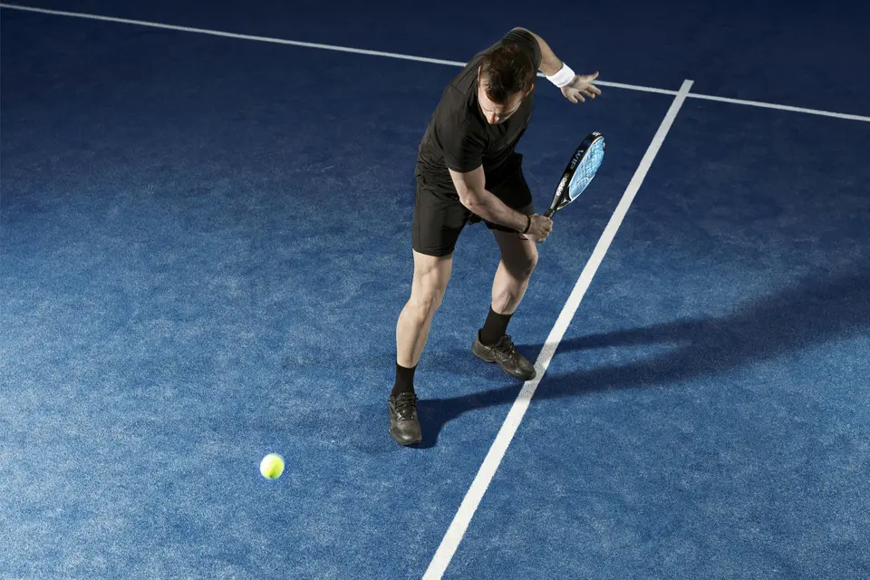 Padel player returning a ball on a blue court.