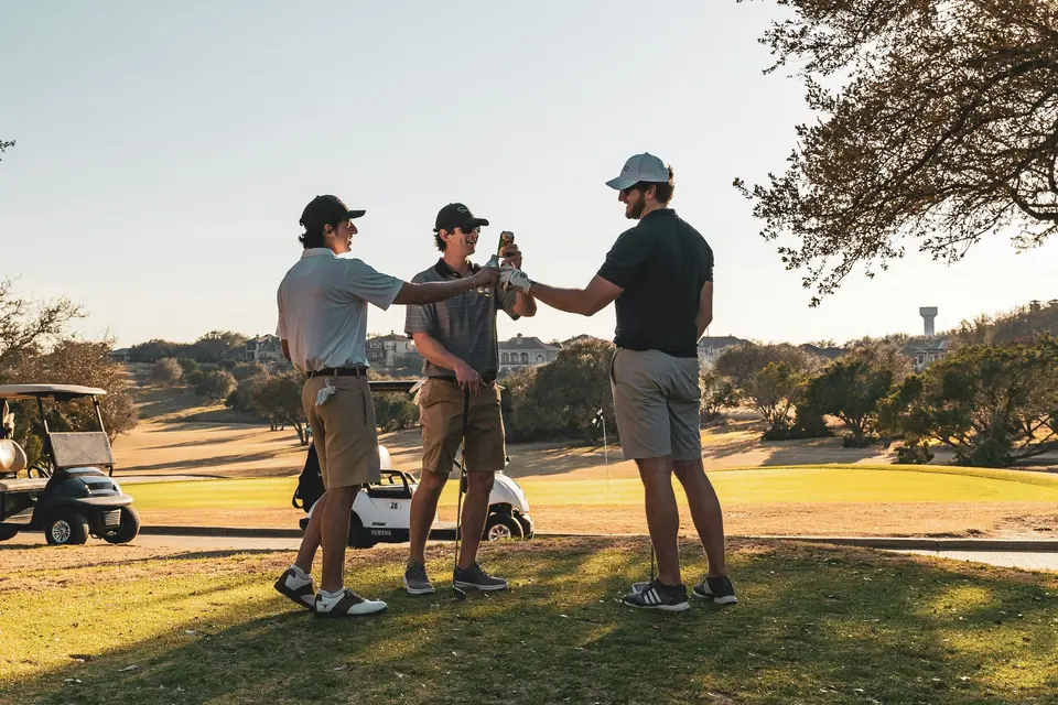 Three golfers celebrating together beside a golf course.